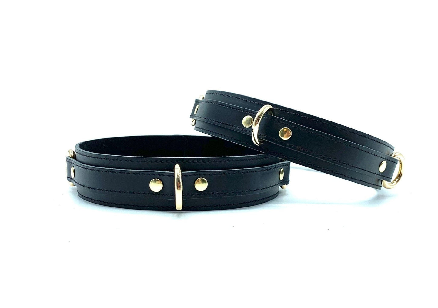 Two thigh cuffs in the Tango Black BDSM Kit, positioned next to each other, crafted from premium black leather with gold hardware, enhancing the BDSM experience with superior bondage features.