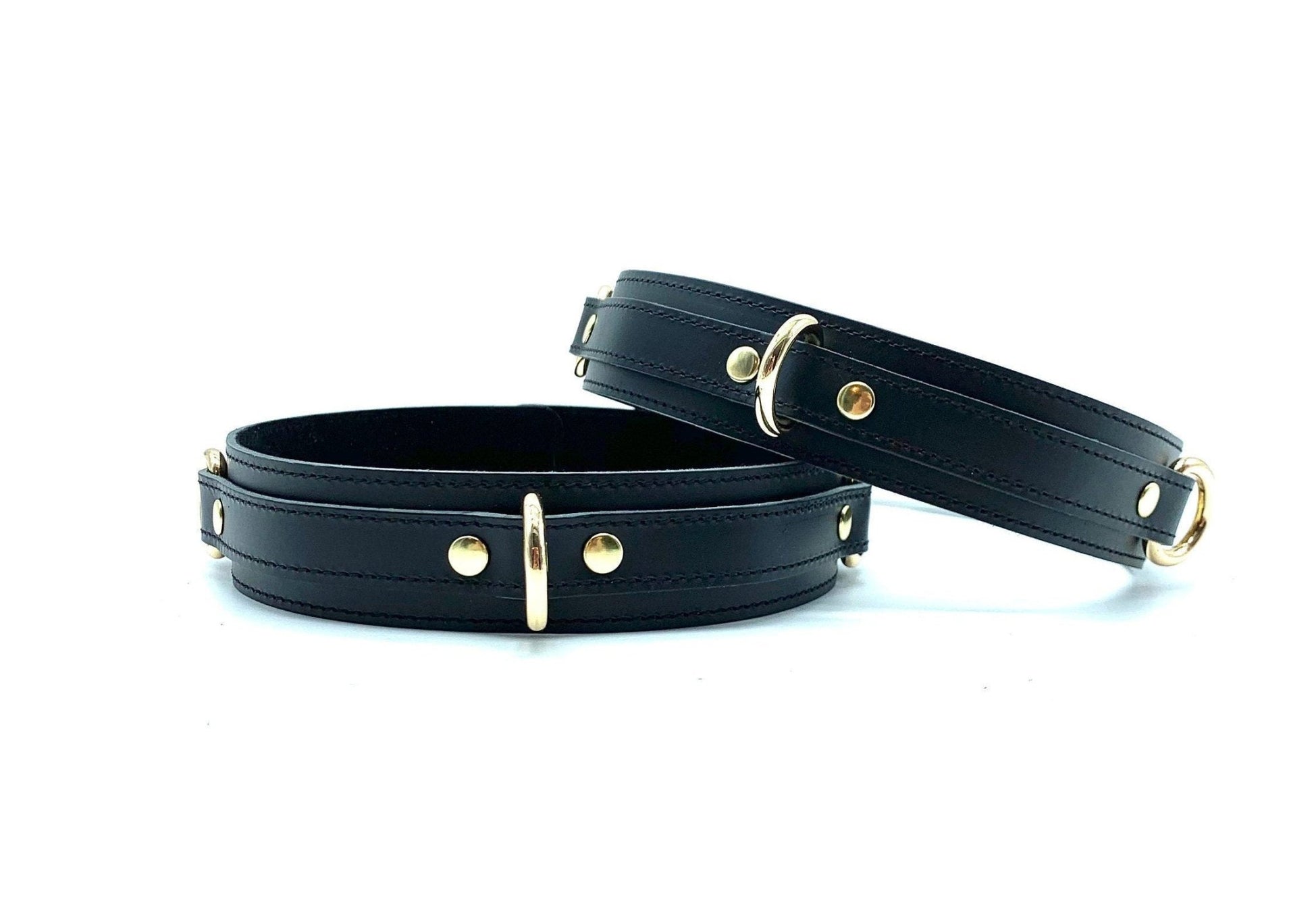 Two thigh cuffs in the Tango Black BDSM Kit, positioned next to each other, crafted from premium black leather with gold hardware, enhancing the BDSM experience with superior bondage features.