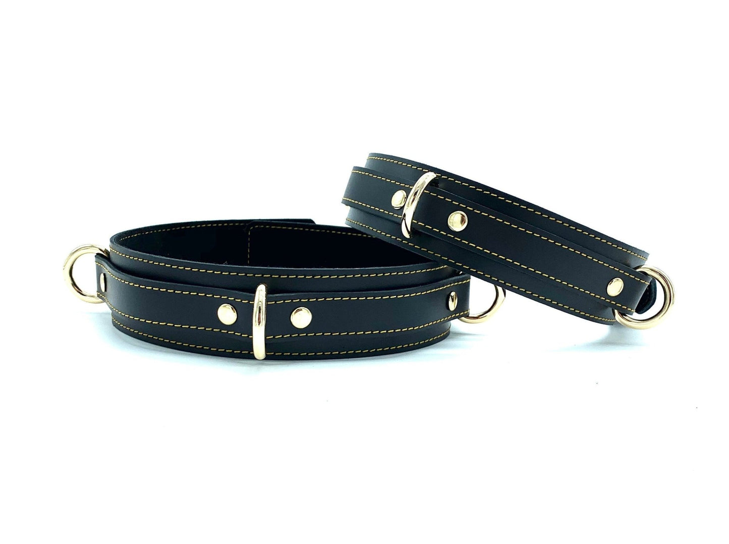 Two thigh cuffs in the Tango Black BDSM Kit, positioned next to each other, crafted from premium black leather with gold stitching and hardware, enhancing the BDSM experience with superior bondage features.