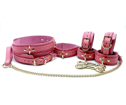Complete Tango Pink BDSM Kit displayed, featuring pink leather and pink suede with gold hardware. The set includes thigh cuffs, a leash with a gold chain, and both ankle and hand cuffs, all crafted with precision and elegance for sophisticated bondage play.
