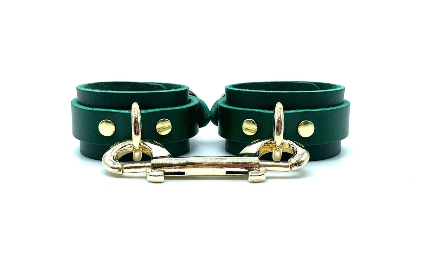 Green leather handcuffs with black suede, linked by striking gold connectors, offering a sophisticated look for BDSM accessories, emphasizing style, comfort, and secure fit, expertly made in the USA.