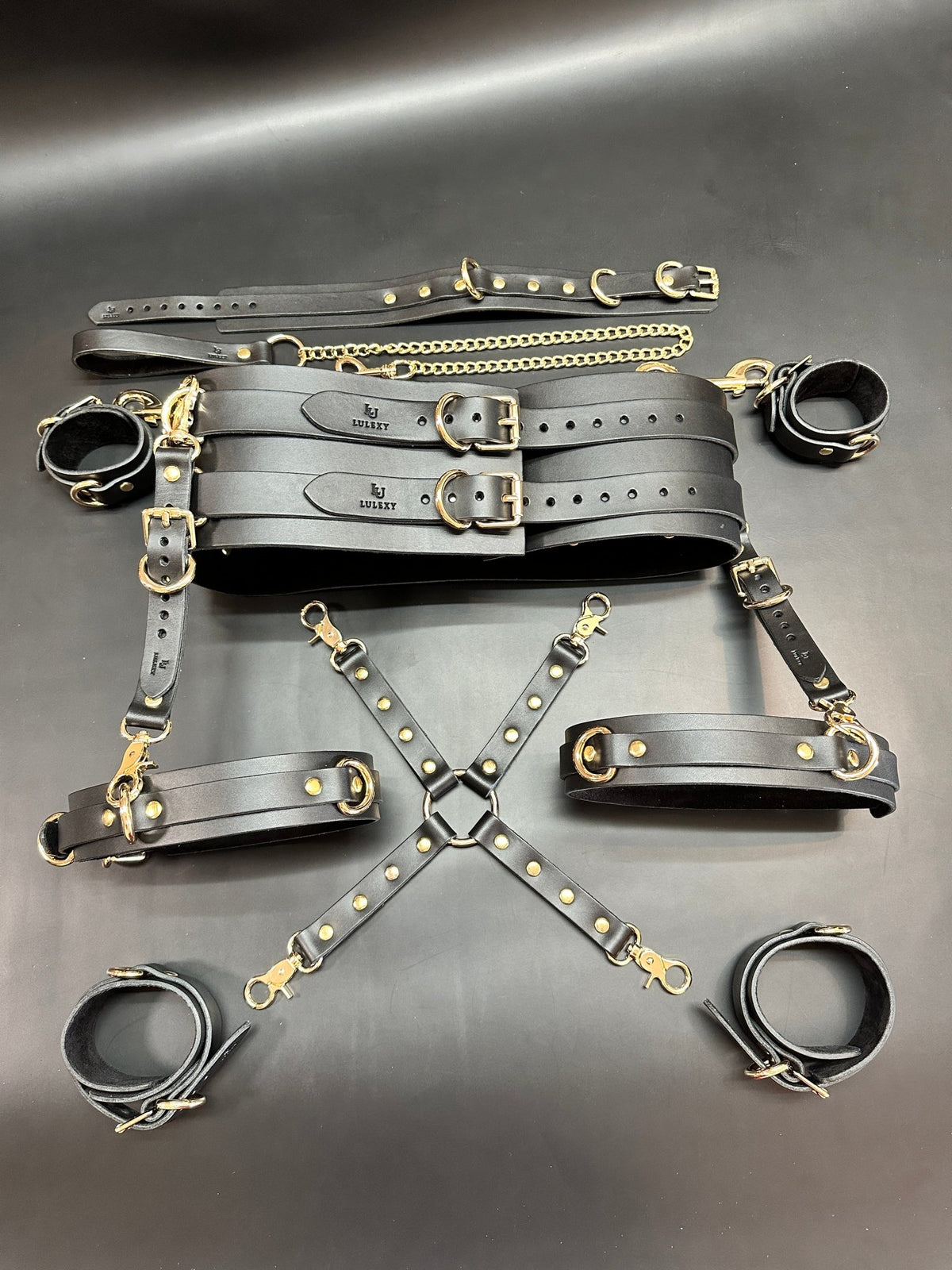 Italian leather bondage kit with cuffs, connectors and gold chain arranged in full set layout