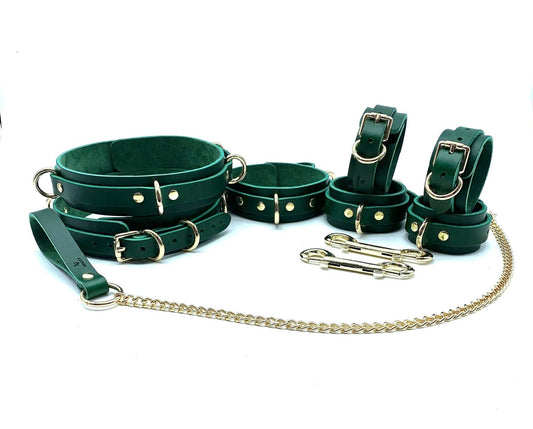Complete Mona Collection BDSM kit displayed, featuring a collar, leash, handcuffs, ankle cuffs, and thigh cuffs, all in green leather with green suede accents and gold hardware. The set includes a gold chain, perfectly integrating luxury and functionality for sophisticated bondage play.