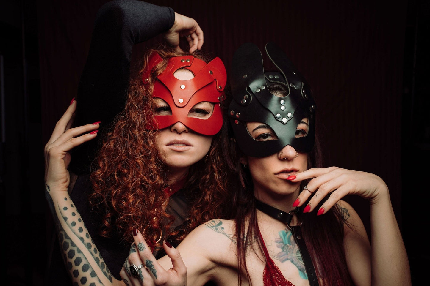 One Red Hair Lady Wearing Red Mask and Another Wearing a Black Bunny Mask with Collar: A lady with striking red hair wearing a vibrant red mask stands beside another lady in a black bunny mask equipped with a collar. The red mask matches her hair color, adding to her vivid and eye-catching look, while the black bunny mask and collar introduce a contrast, emphasizing a playful yet bold aesthetic.
