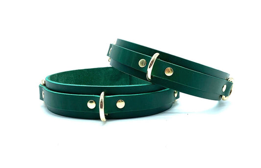 Lulexy Front view of luxurious Mona Green Italian leather BDSM bondage thigh cuffs, showcasing deep green leather with prominent D-rings attached, highlighting the cuffs' opulent design against a neutral backdrop.