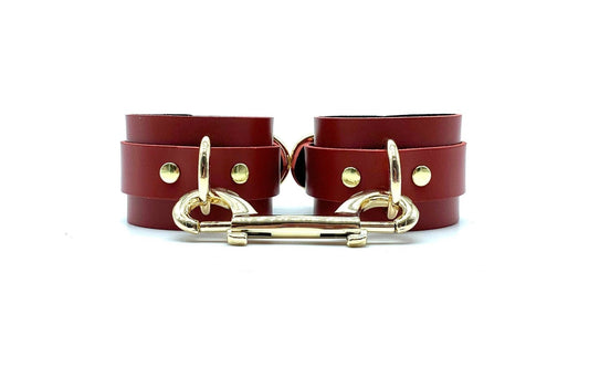 Front view of red leather cuffs with black suede lining, connected side by side with a gold connector, displaying rich contrast and elegant gold hardware, ideal for those seeking a stylish and secure BDSM accessory.