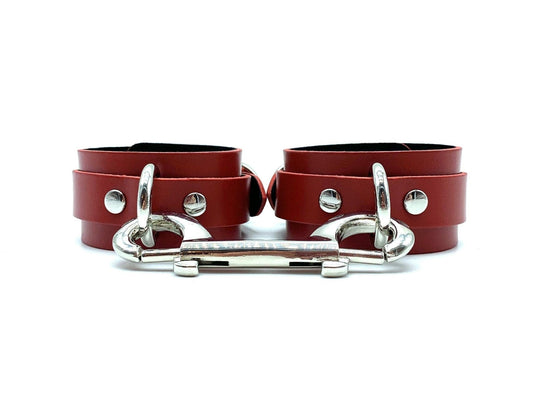 Red leather handcuffs with black suede lining, connected by a durable silver connector, showcasing elegant design and robust construction ideal for BDSM play, reflecting high-quality craftsmanship made in the USA.