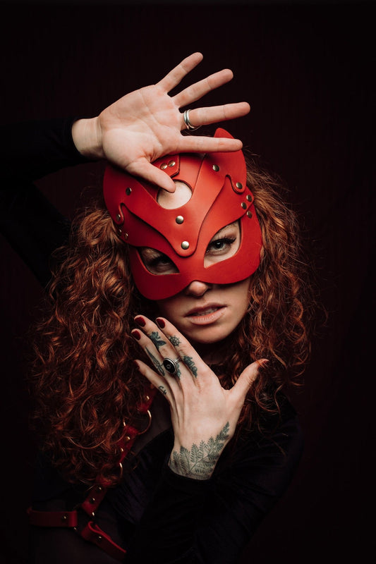  Lady with vibrant red hair wearing a sleek cat mask, featuring elegant contours and eye cutouts that accentuate her mysterious expression. The mask complements her striking hair color, adding an air of mystique.