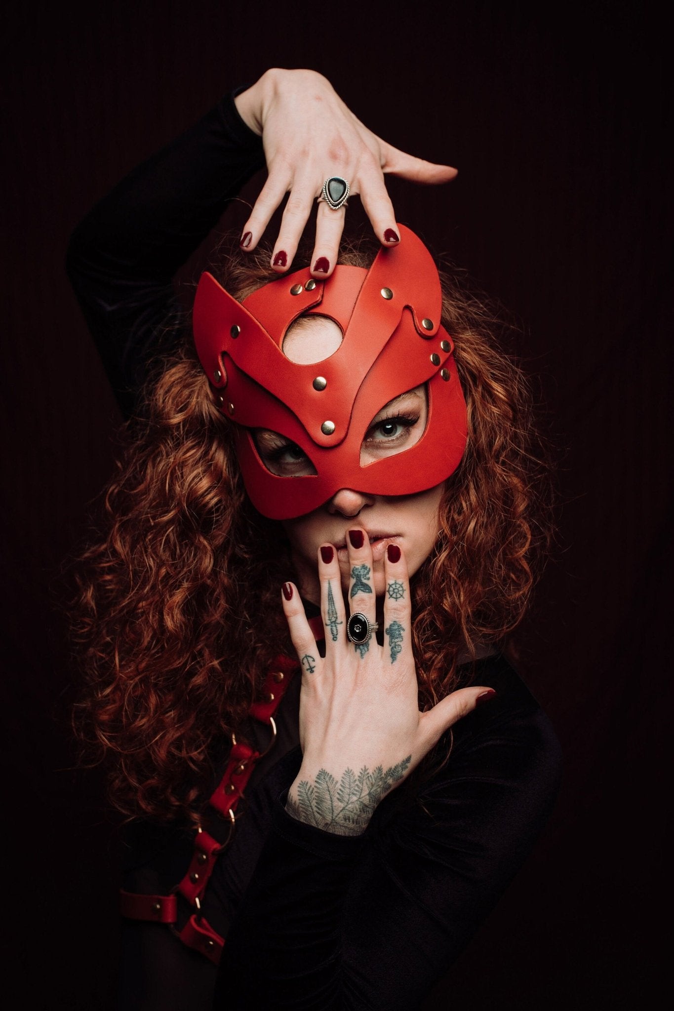 Lady with vibrant red hair wearing a sleek cat mask, featuring elegant contours and eye cutouts that accentuate her mysterious expression. The mask complements her striking hair color, adding an air of mystique.