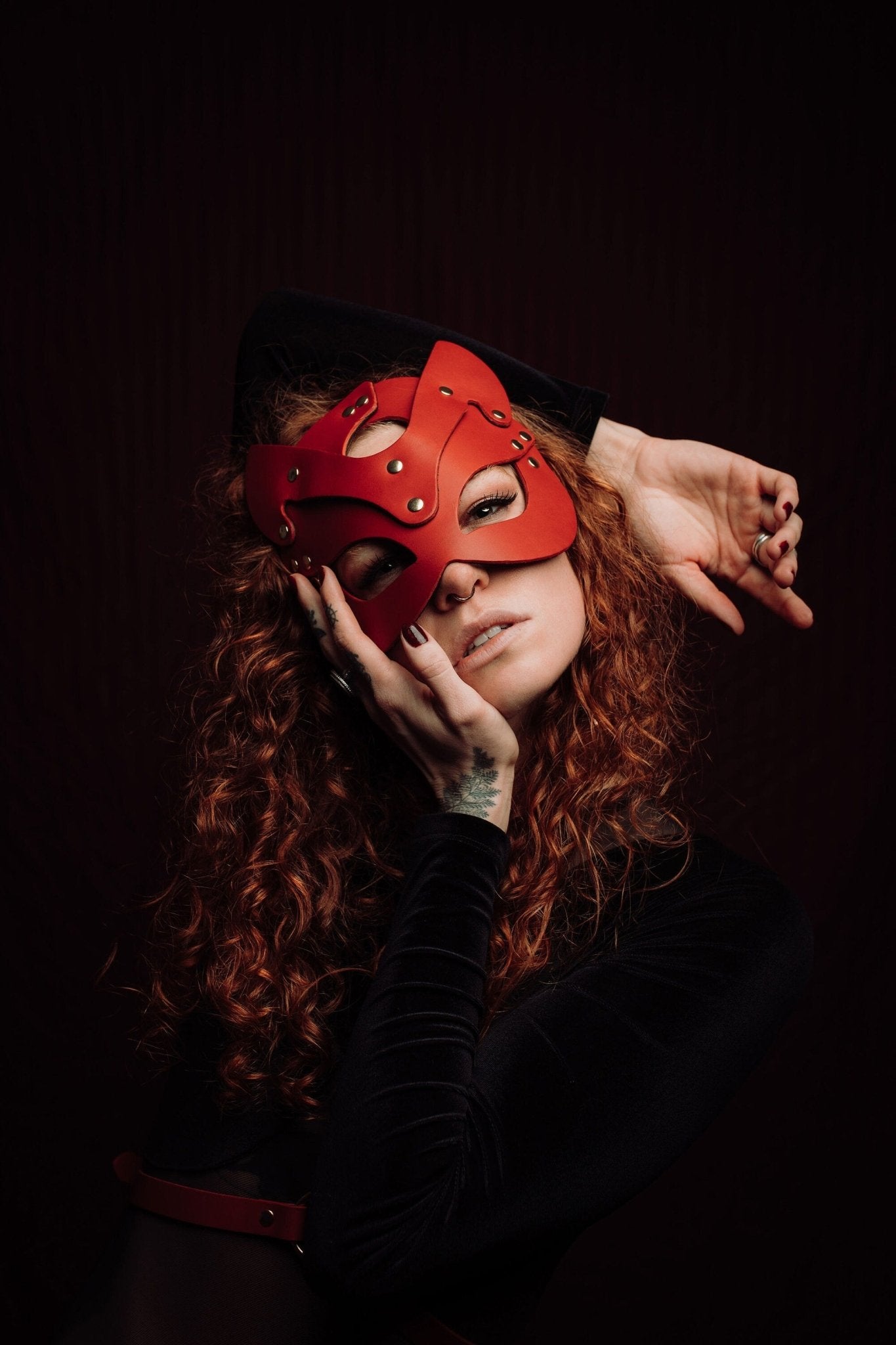 Lady with vibrant red hair wearing a sleek cat mask, featuring elegant contours and eye cutouts that accentuate her mysterious expression. The mask complements her striking hair color, adding an air of mystique.