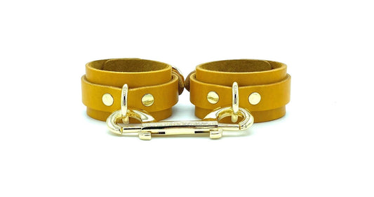 Front view of yellow Italian leather handcuffs with matching yellow suede lining, featuring luxurious gold hardware and a gold connector, designed for elegance and durability in BDSM play, handcrafted in the USA.