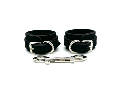 Italian black suede BDSM bondage cuffs made in the USA, featuring sleek cuffs positioned side by side, adorned with opulent gold hardware and matching connectors, designed to exude both elegance and security in intimate bondage play.