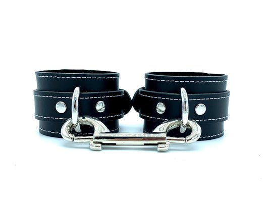 Italian leather and suede BDSM bondage 2" cuffs made in the USA, showcasing Tango black leather and black suede cuffs with contrasting white stitching and sleek silver hardware, presented in a front view with a silver connector, combining style and functionality for bondage enthusiasts.