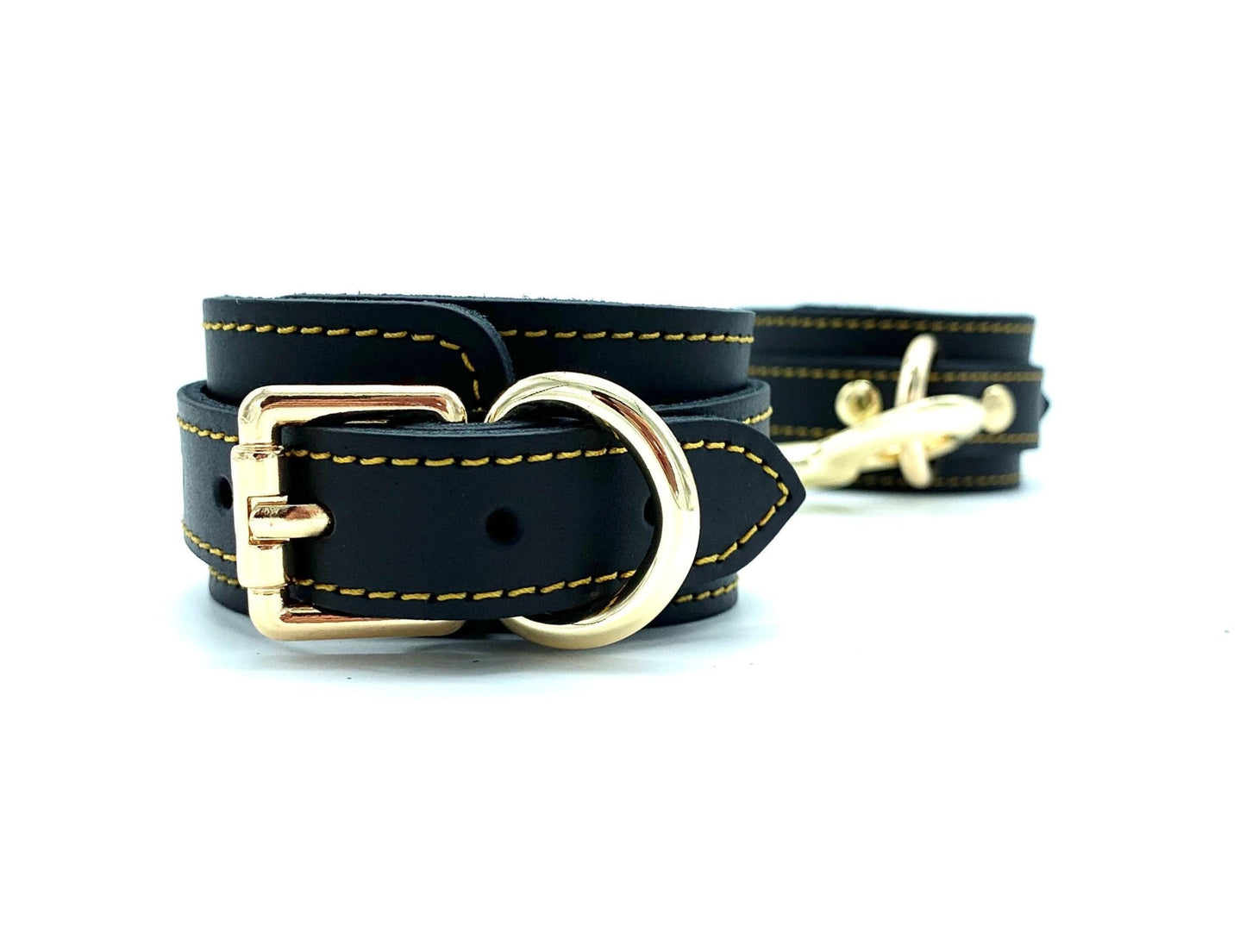 Pair of Italian leather and suede BDSM bondage cuffs made in the USA, Tango black cuffs connected sideways, highlighting their sleek design and secure fit, enhanced by the presence of gold hardware for a luxurious touch.