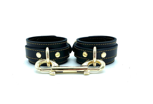 Italian leather BDSM bondage cuffs made in the USA, showcasing Tango black leather and black suede cuffs with intricate gold stitching, accompanied by gold hardware and a gold connector, radiating elegance and quality craftsmanship.