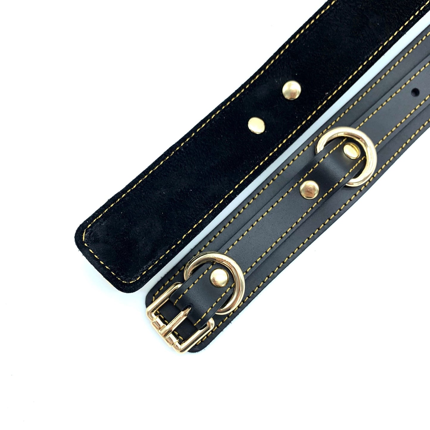 Italian leather and suede BDSM bondage cuffs made in the USA, Tango black cuffs lying down to display their combination of black leather and black suede with intricate gold stitching, embodying sophistication and attention to detail.