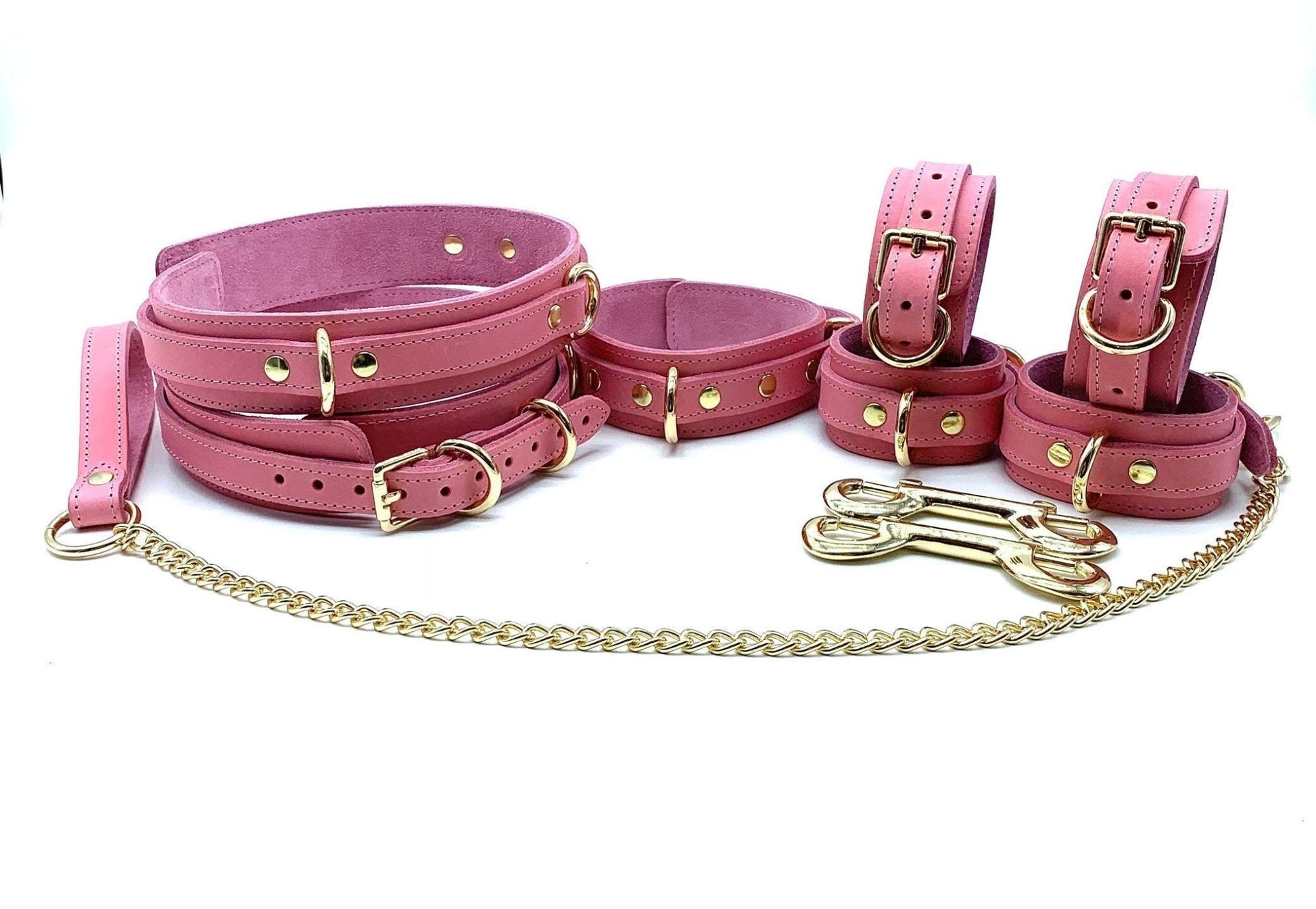 An arrangement of seven Tango Pink Italian leather BDSM bondage thigh cuffs, collars and leash, hand cuffs, ankle cuffs displayed together to showcase their consistent pink hue and gold hardware, emphasizing the complete set.