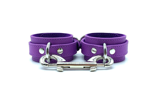 Italian leather BDSM bondage cuffs made in the USA, showcasing Tango purple leather and purple suede cuffs with a front view, accented by sleek silver hardware and a silver connector, epitomizing luxury and durability.