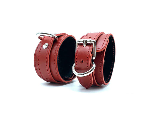 Italian leather BDSM bondage cuffs made in the USA, featuring red leather and black suede, displayed next to each other with sleek silver hardware, highlighting the luxurious materials and precision craftsmanship.