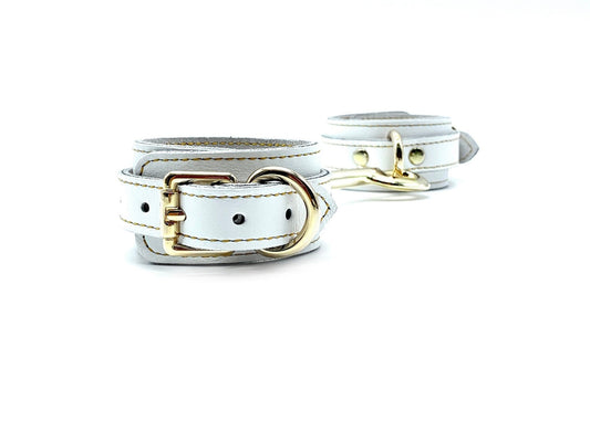 Italian white leather and suede BDSM bondage cuffs made in the USA, connected sideways by a sleek connector adorned with intricate gold stitching, showcasing exquisite craftsmanship and luxurious detailing for indulgent bondage play.