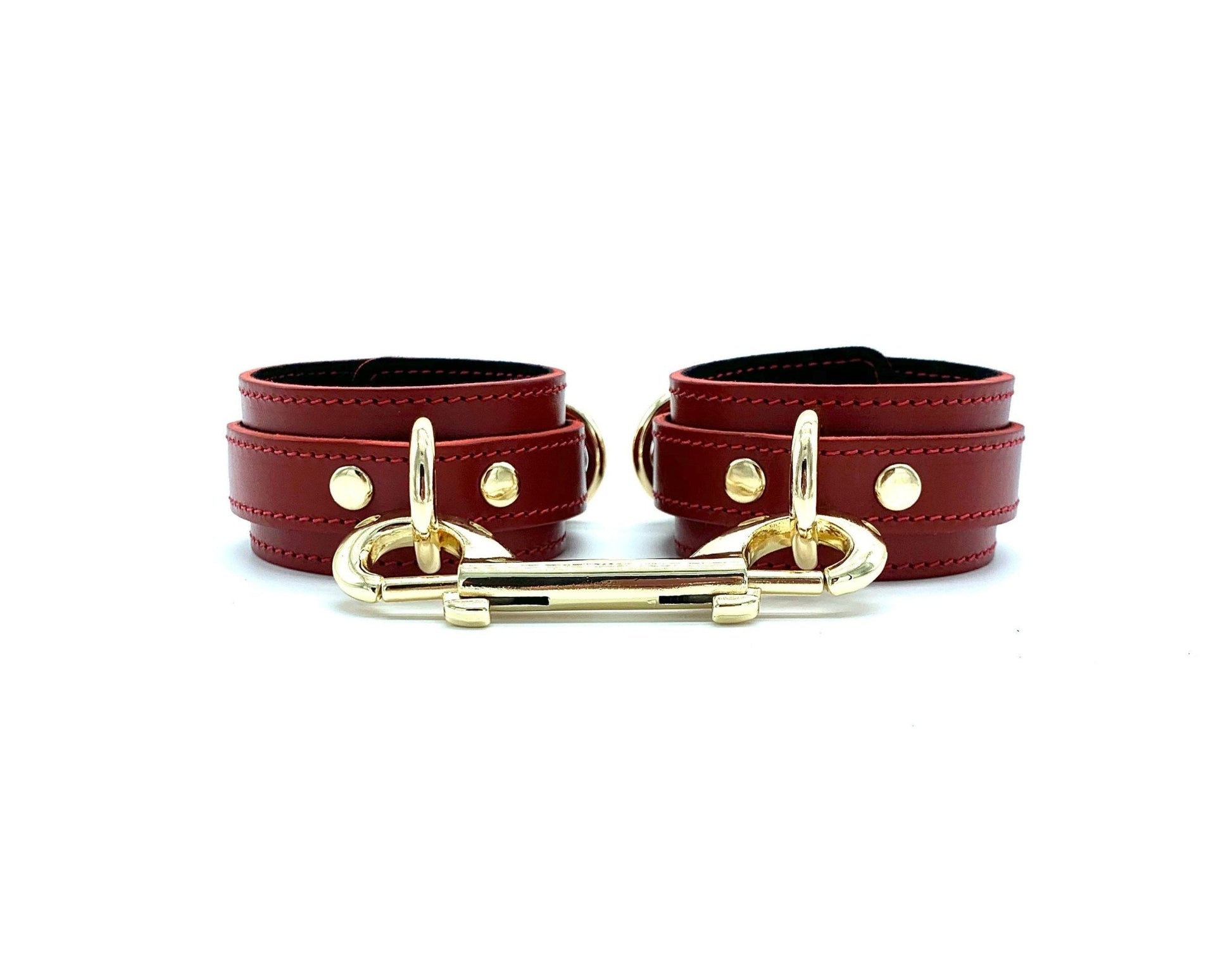 Set of four red leather cuffs displayed next to each other, connected by a gold connector, accentuating the luxurious and custom BDSM gear.