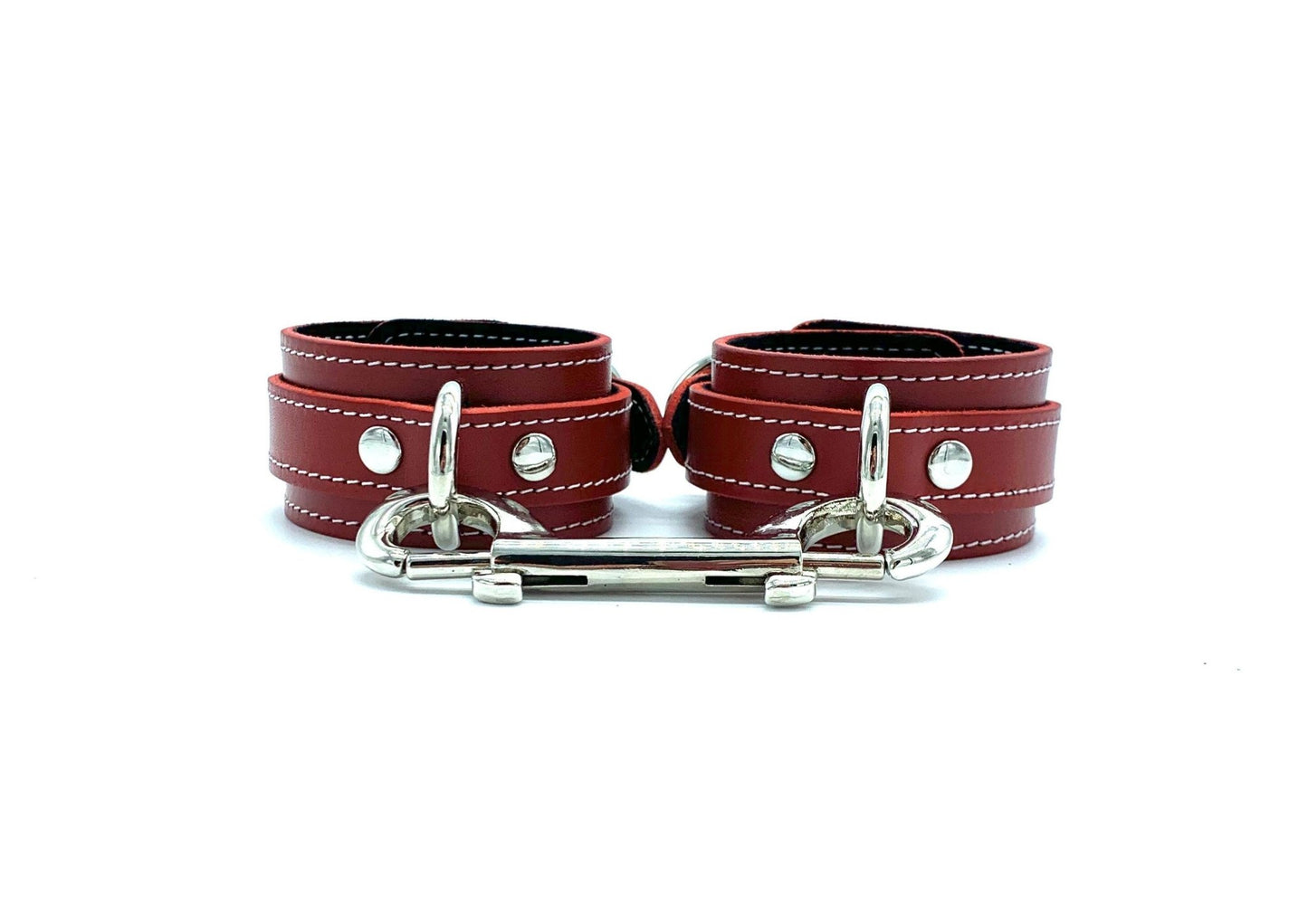 Pair of red leather handcuffs from the Tango Red BDSM Kit, connected by a silver hardware connector. The cuffs are accented with black suede and white stitching, designed for secure and stylish restraint in BDSM play.