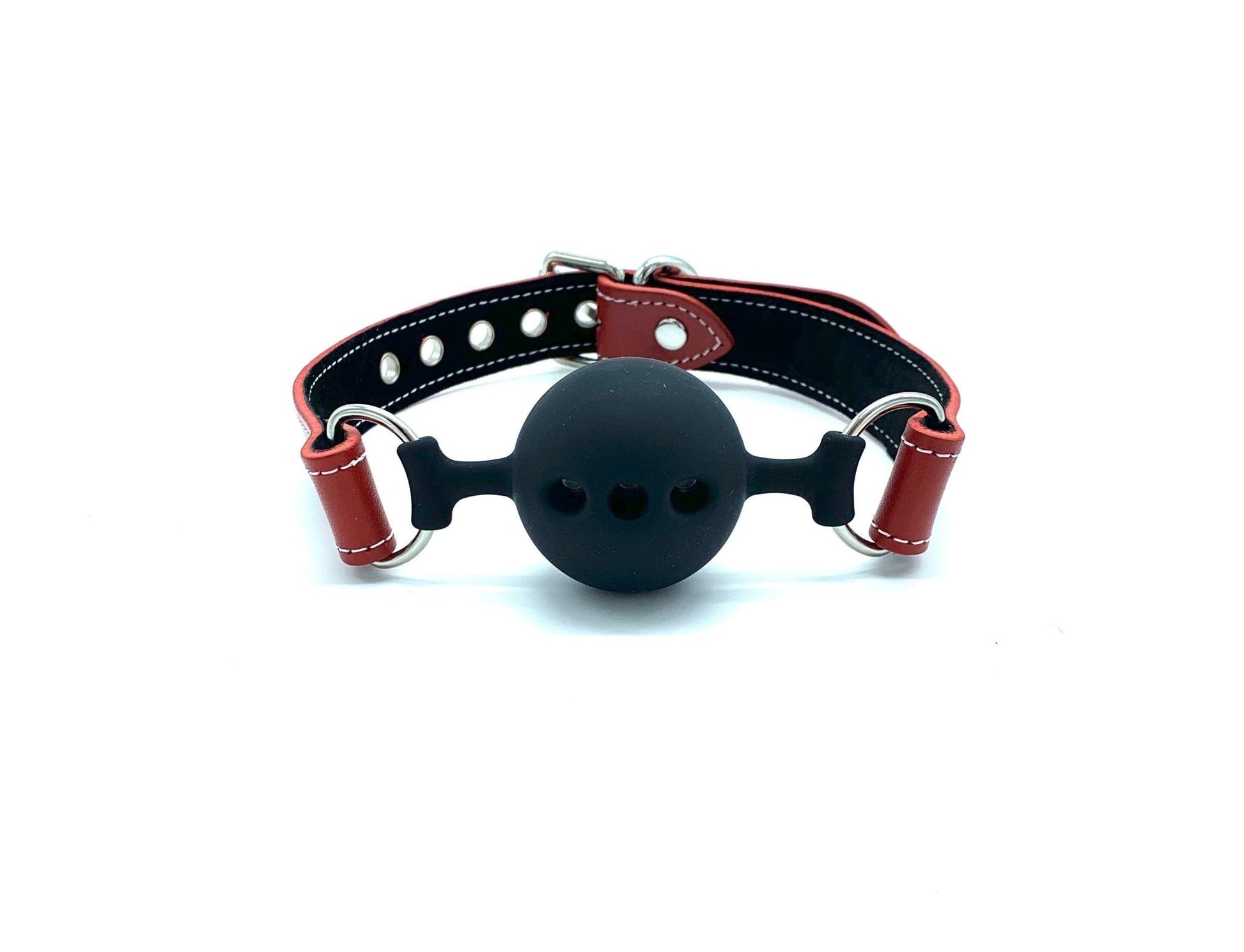 "Close-up view of the Tango Red BDSM Kit items including a ball gag, a collar with a detachable leash, and a pair of handcuffs, one positioned vertically above the other. Each item is made from red leather with black suede accents and white stitching, finished with silver hardware, showcasing detailed craftsmanship and high-quality materials