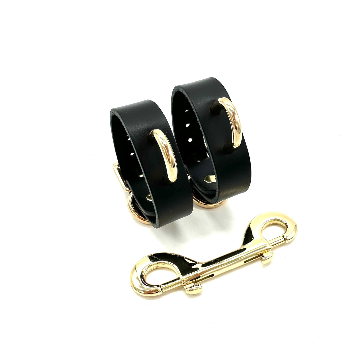 Slim black leather cuffs with centered shiny gold D ring and double end snap hook connector