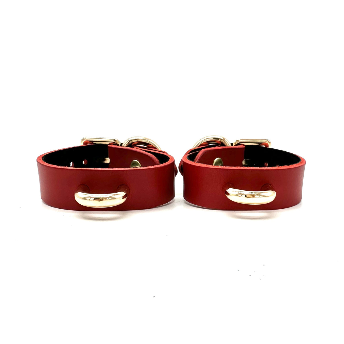 A pair of slim red leather cuffs with centered minimalistic gold D ring. 