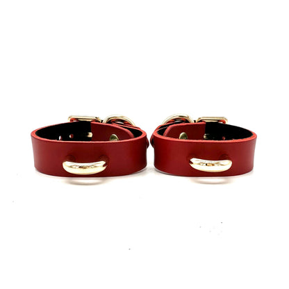 A pair of slim red leather cuffs with centered minimalistic gold D ring. 
