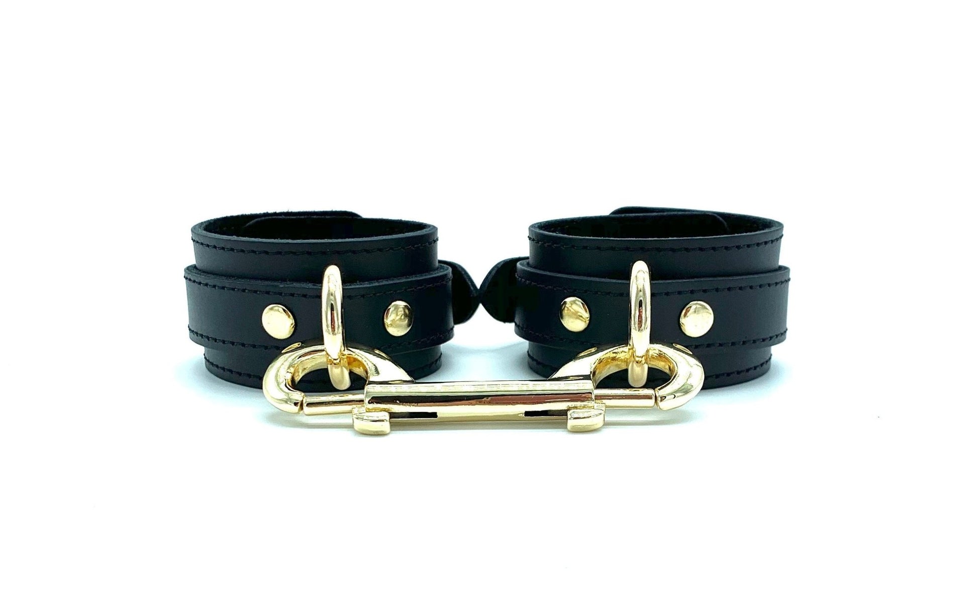 A pair of black leather ankle cuffs with gold D rings and double ended snap hook used to connect them.
