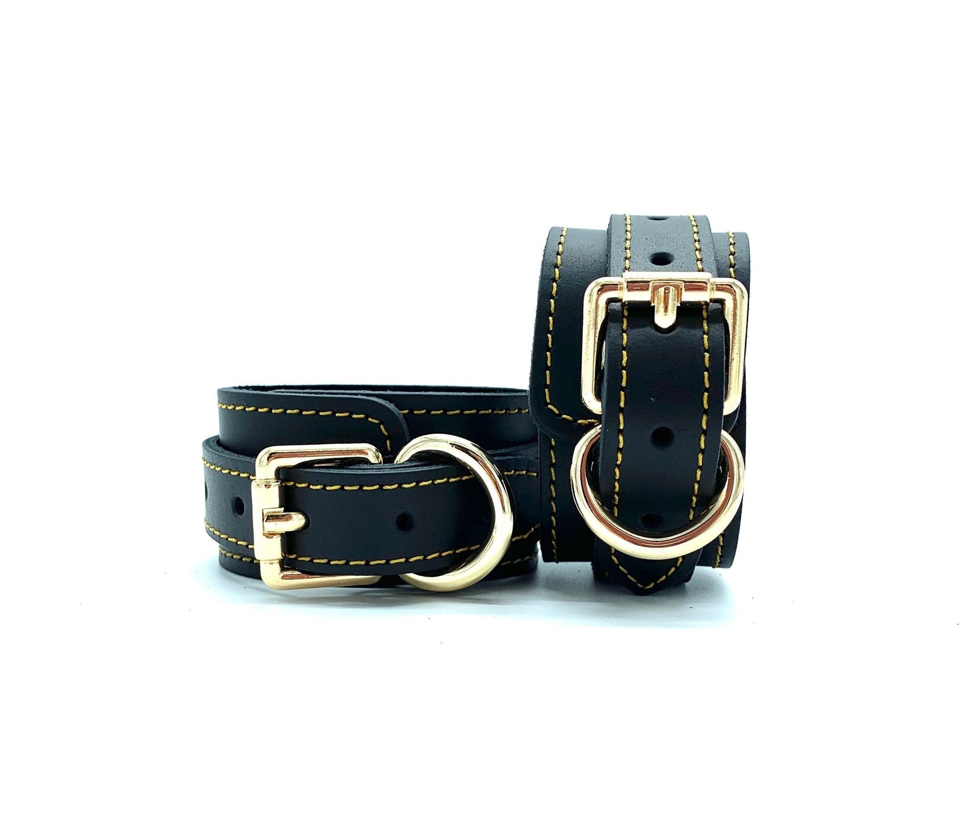 Close up of black leather handcuffs featuring detailed gold stitching and elegant gold buckle.