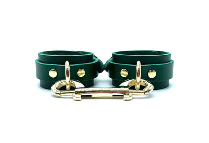 Pair of green leather handcuffs from the Mona Set, lying next to each other, highlighting the gold connectors and the exquisite craftsmanship. These cuffs not only secure but also add a visually appealing aspect to the collection.