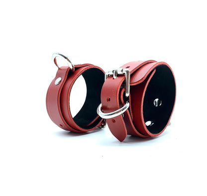 Red leather handcuffs with black suede lining, standing adjacent to each other, featuring sleek silver hardware that emphasizes their luxury and durability, perfect for stylish BDSM enthusiasts.