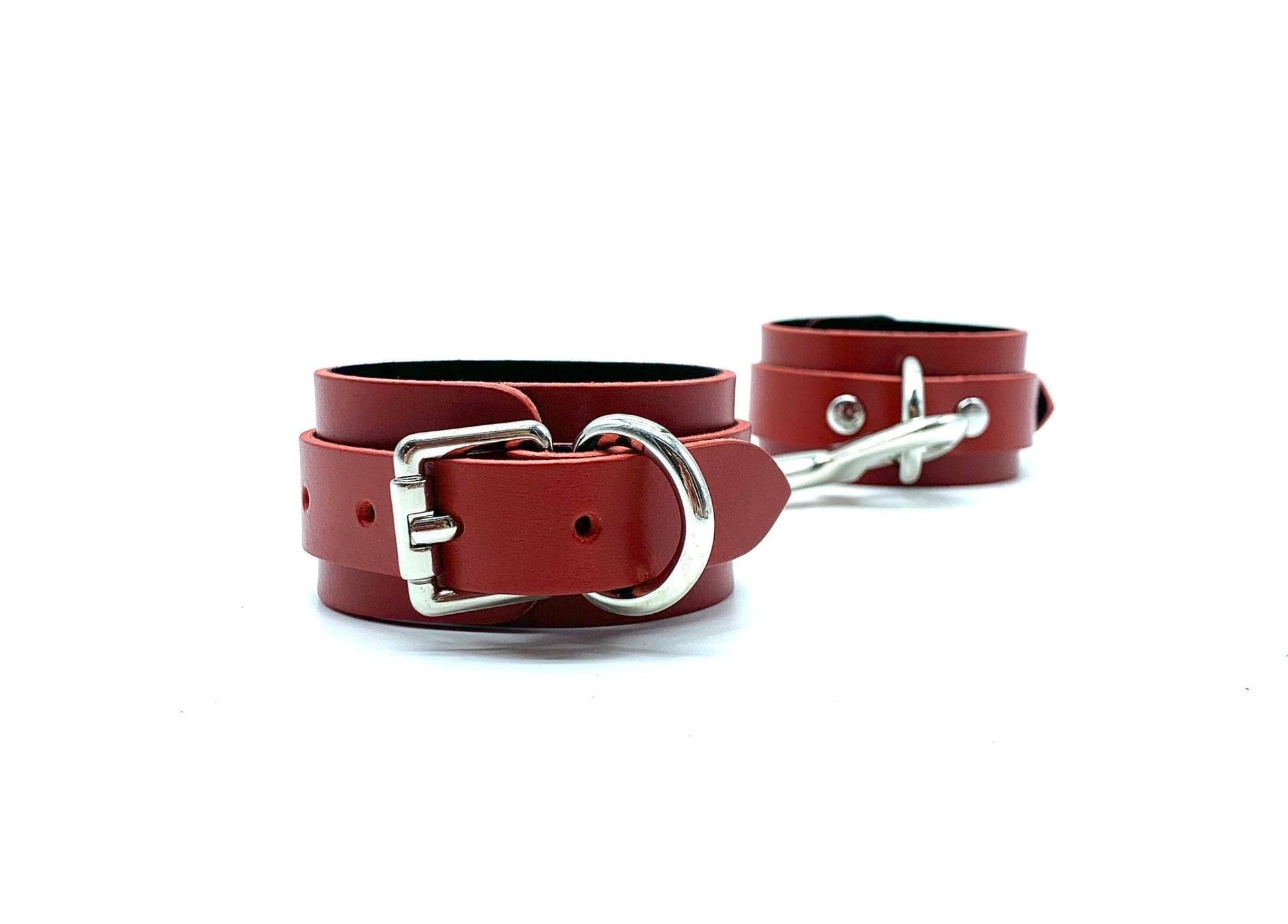 Pair of red leather handcuffs with black suede, displayed side by side, highlighting their shiny silver buckles, designed for both aesthetic appeal and functional bondage use, crafted with precision in the USA.