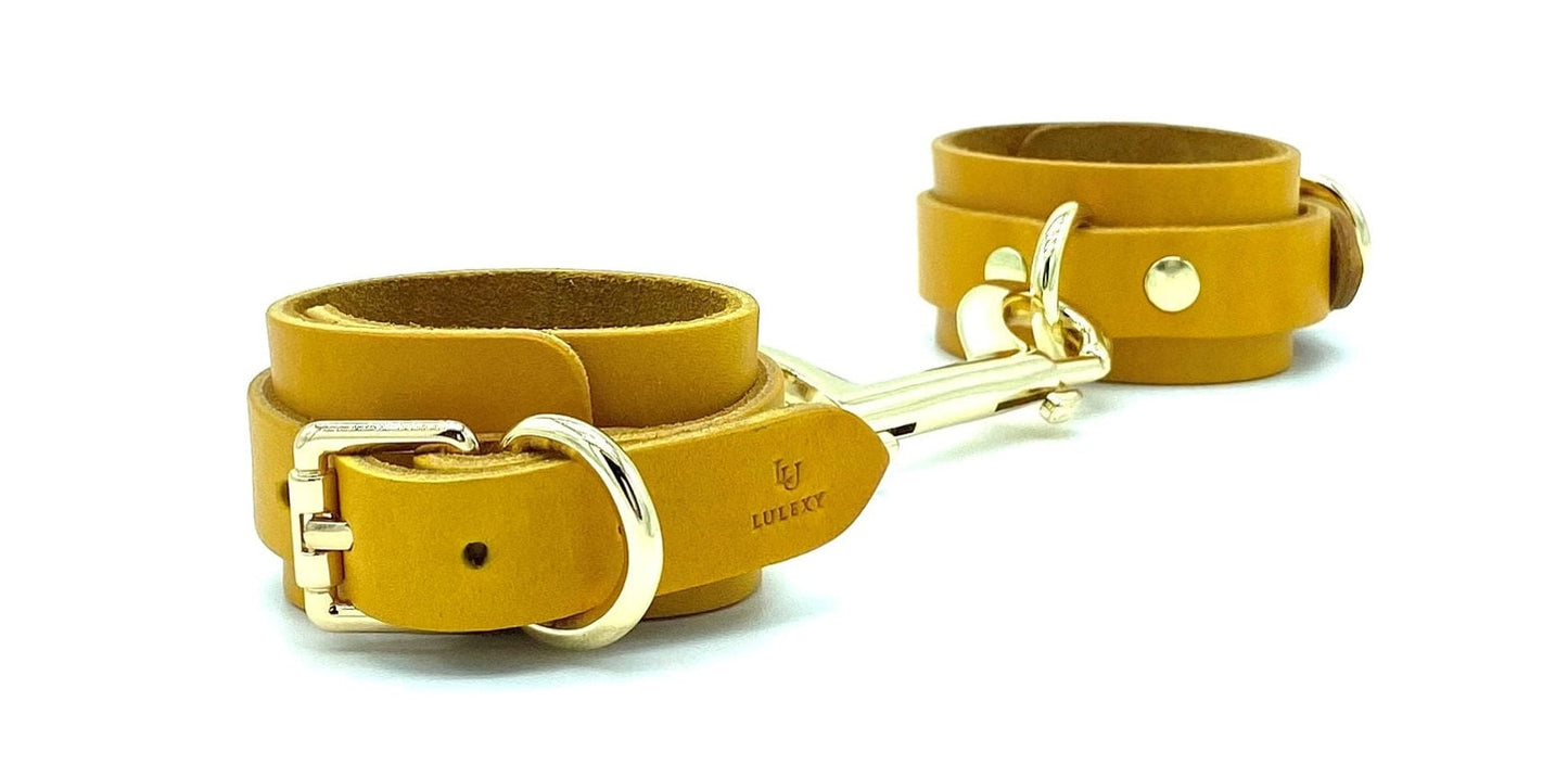 Yellow Italian leather handcuffs connected by a gold connector, showcasing a uniform yellow suede lining and elegant gold hardware, exemplifying luxury and security for high-end BDSM play, meticulously crafted in the USA.