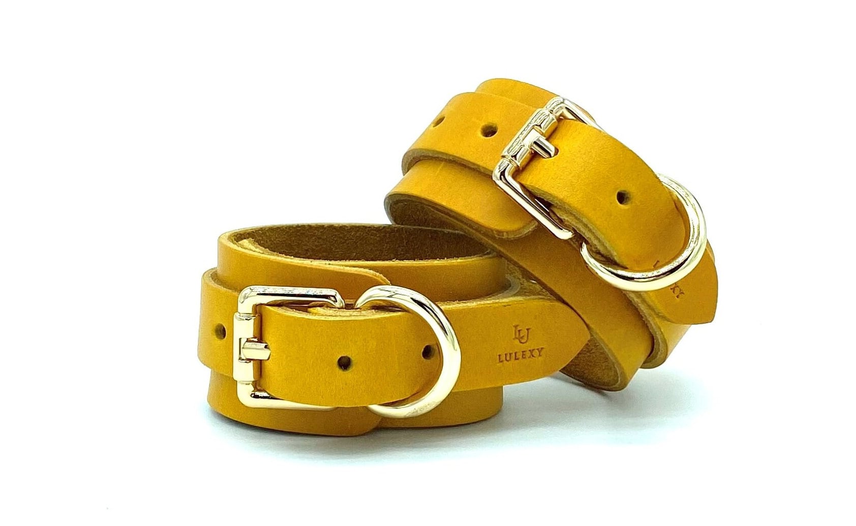 Back side view of yellow Italian leather handcuffs stacked on top of each other, displaying intricate gold buckles, emphasizing the premium construction and stylish design suited for sophisticated BDSM enthusiasts.