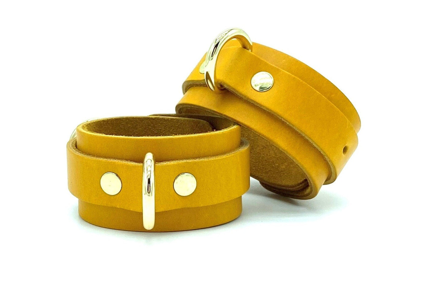 Stack of yellow Italian leather handcuffs with yellow suede, shown in a front view that highlights their consistent color and quality gold hardware, offering a visually appealing and functional bondage accessory.