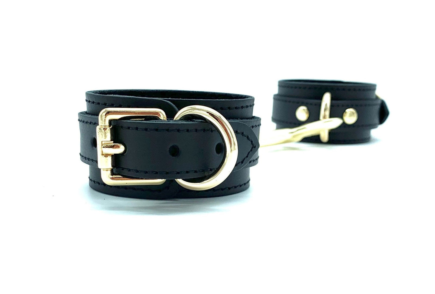 Side view of connected Tango black leather cuffs, highlighting the detailed gold buckle and precise black stitching, emphasizing the premium quality and durability designed for enhanced bondage experiences.