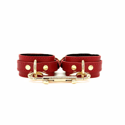 Red leather handcuffs with gold hardware, front view of adjustable wrist cuffs