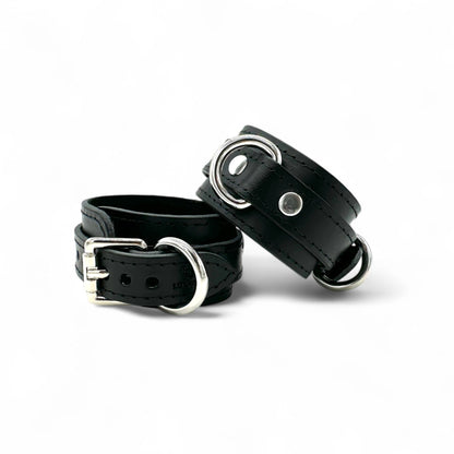 Black leather handcuffs close up with silver hardware, rivet detail and structured design