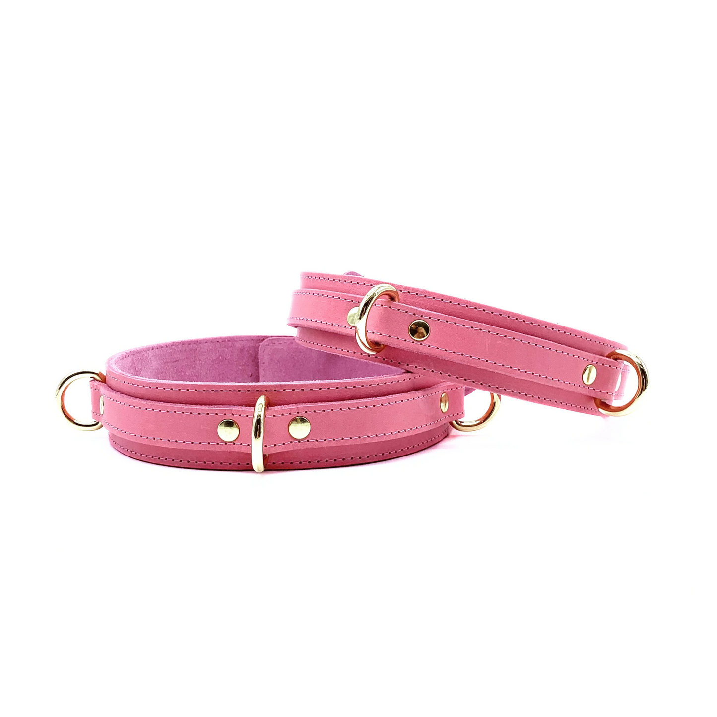 Pink leather thigh cuffs from Tango collection featuring various gold D rings for attachment points on white background.