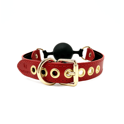 Close-up of gold buckle on red leather ball gag strap with metal eyelets for size adjustment