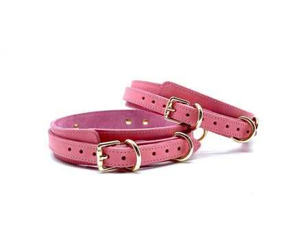 Back view of Tango Pink Italian leather BDSM bondage thigh cuffs, displaying the craftsmanship of the gold buckles and the stitching detail on the pink leather, set on a contrasting white backdrop.